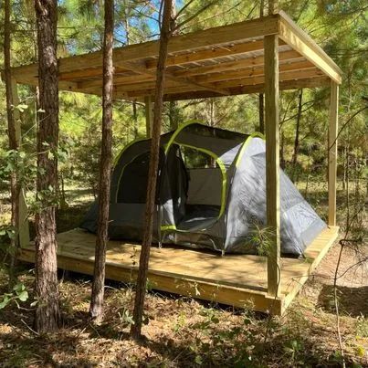 Gray tent on a raised wooden platform under a simple roof in a wooded campsite