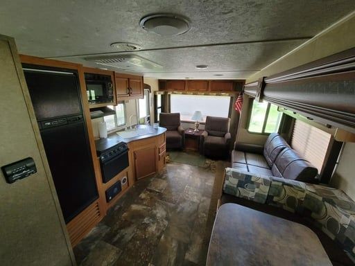Interior of an RV with kitchenette, dinette, and sofa in warm wood tones.