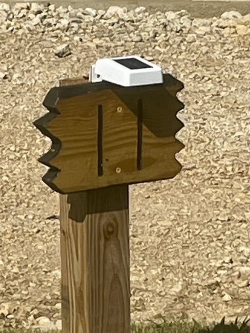 Wooden signpost with a white solar sensor mounted on top in a rocky outdoor area