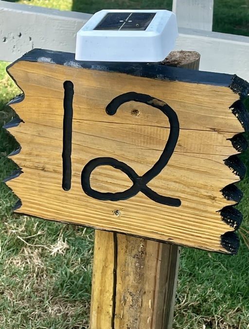 Wooden sign with the number 12 painted in black, mounted on a post outdoors.