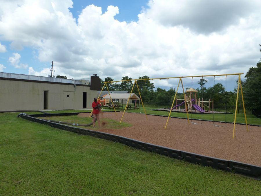 A man is sweeping the grass in front of a playground