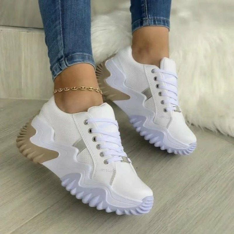 Zapatillas blancas con acento beige sobre una superficie de color claro, persona que lleva jeans.