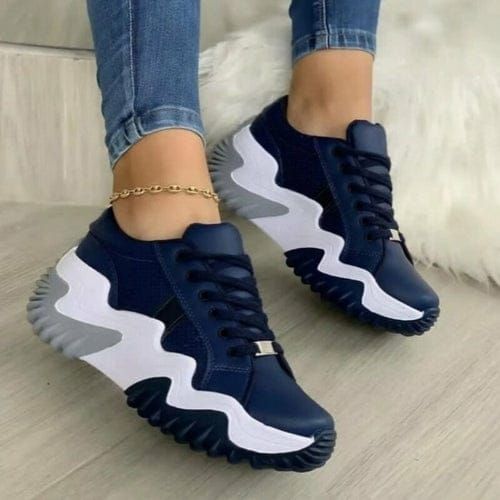 Zapatillas azul marino y blancas en los pies de una persona, pulsera de tobillo dorada, jeans.