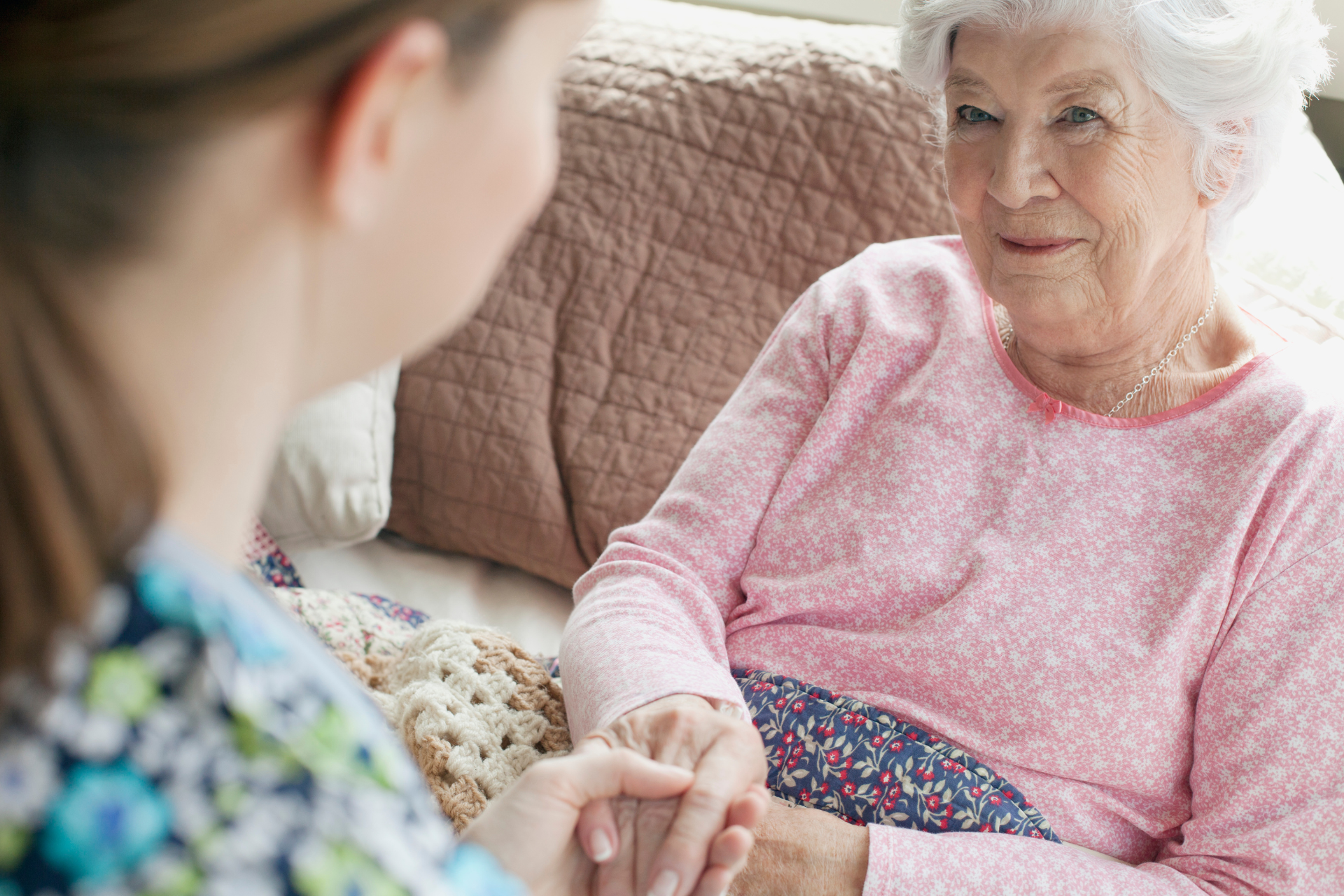 an elderly woman is sitting on a couch holding a nurse 's hand showing compassion in homecare