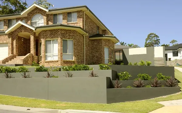 Two-story brick home with a terraced garden bed and a blue sky.