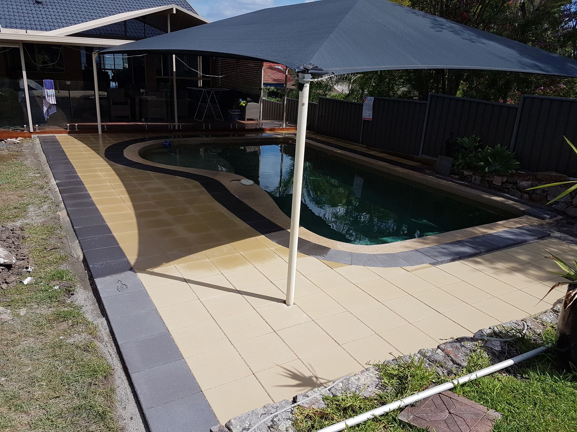 Pool deck with tan, gray, and black pavers around a pool — Creating Eden Landscaping In Warners Bay, NSW