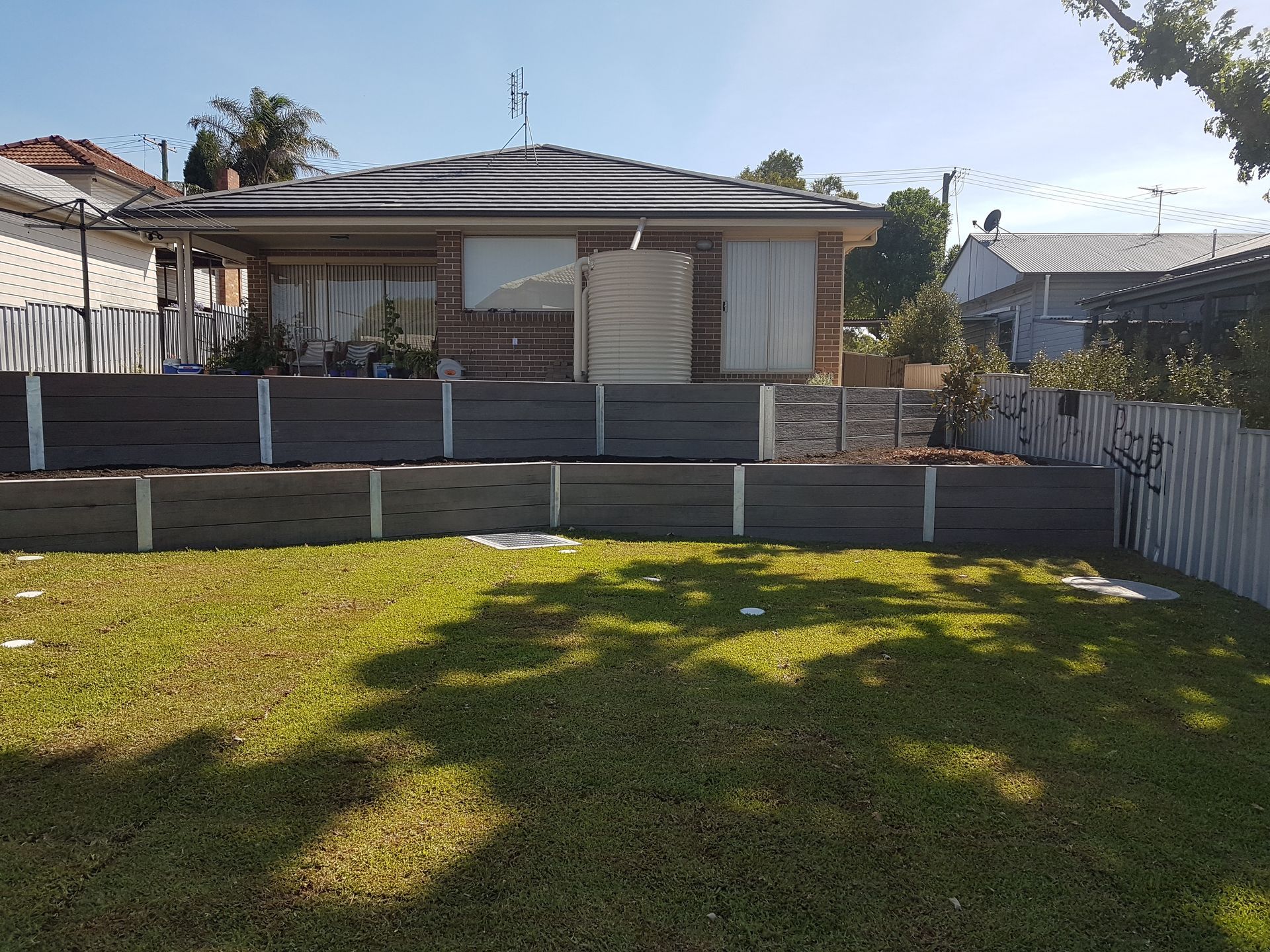 A house with a tiered retaining wall and a green lawn. The house is brick.