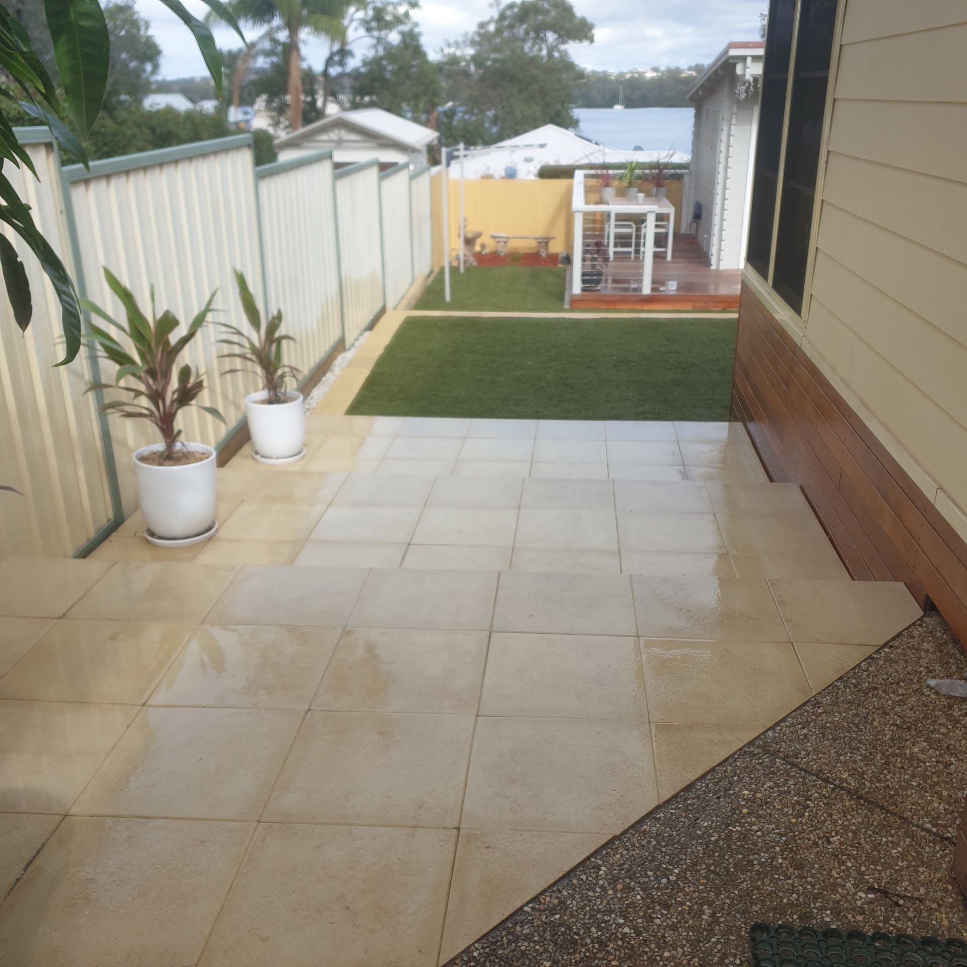 Patio with tile flooring, potted plants, and a small lawn with a white fence.