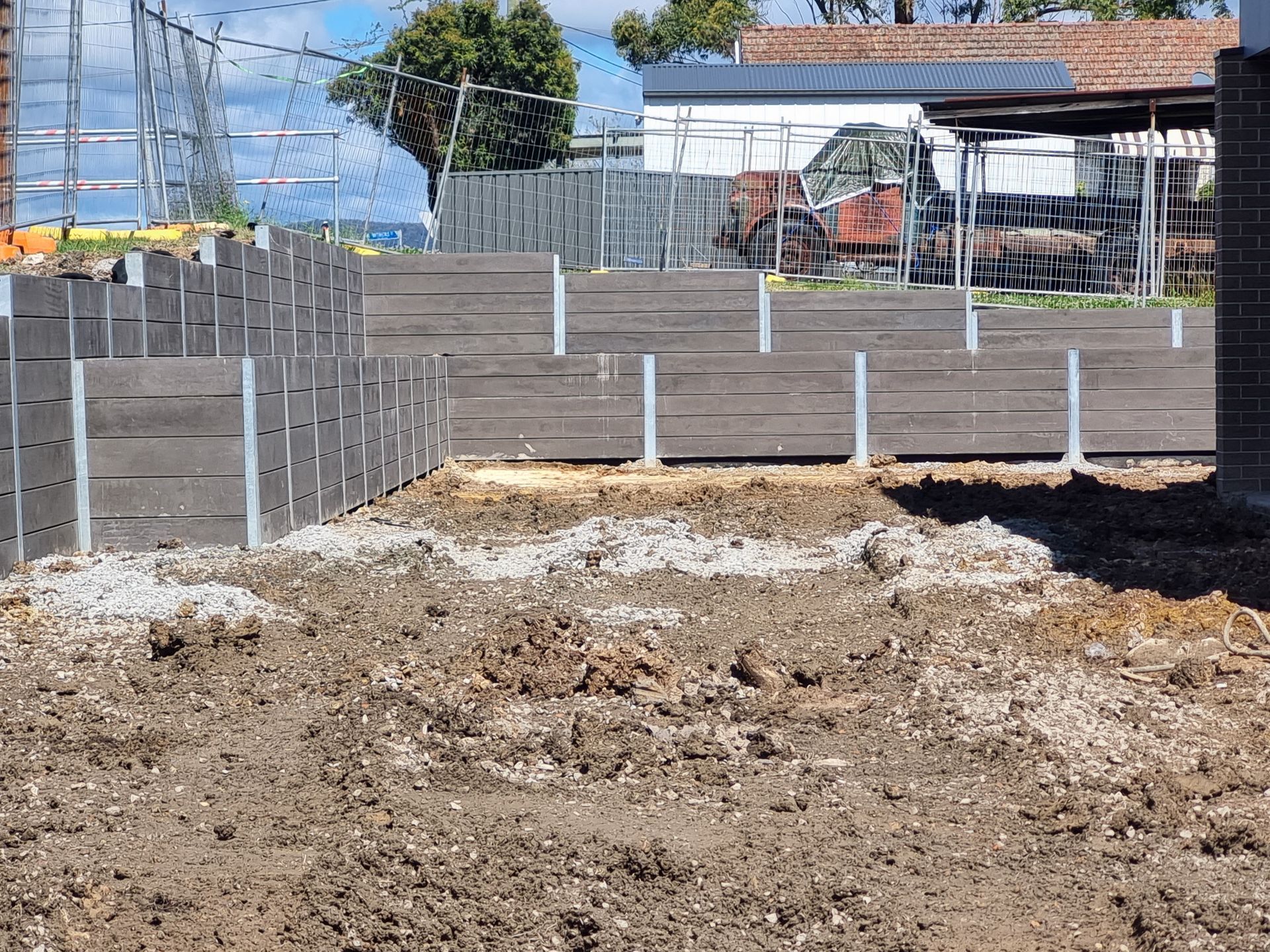 A construction site with a retaining wall made of timber and metal posts, in a dirt yard.
