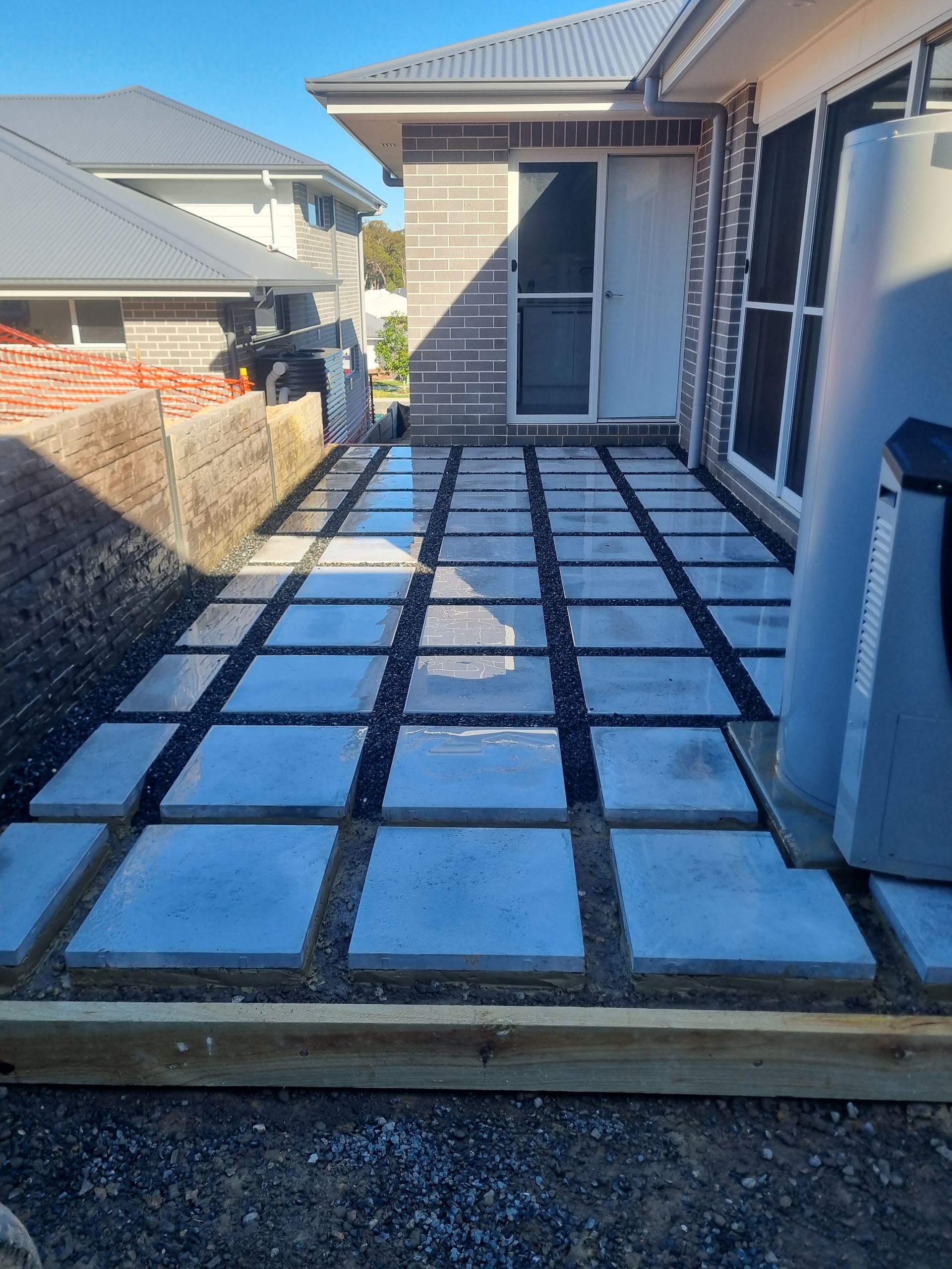 Concrete pavers laid with black space between on a backyard patio near a house.