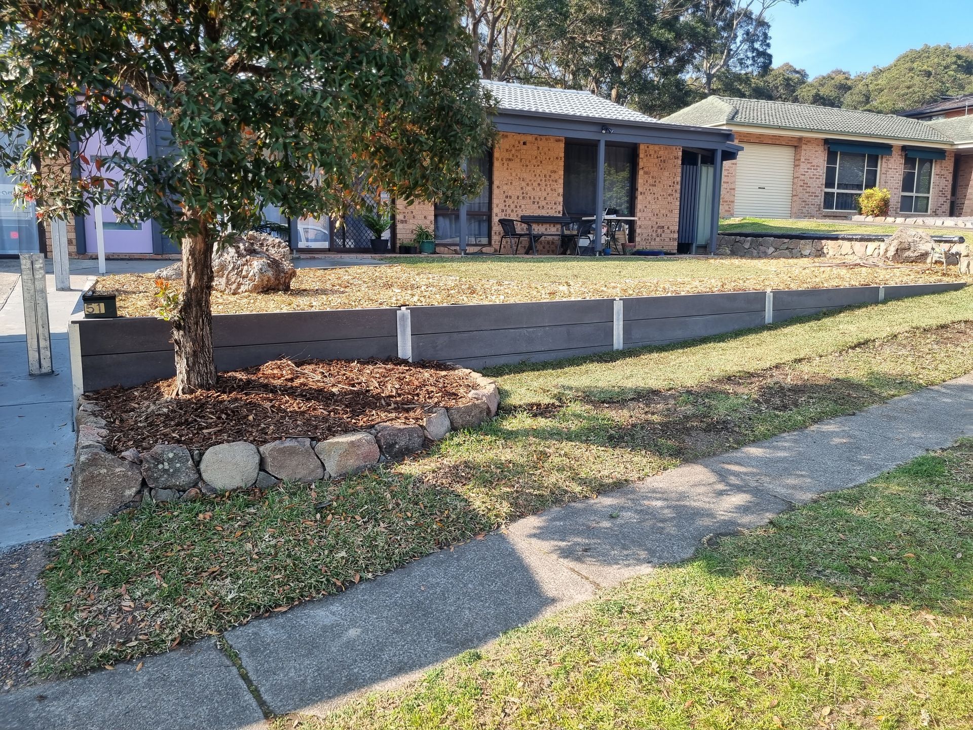 A house with a low retaining wall in front yard, small tree with rocks and mulch.