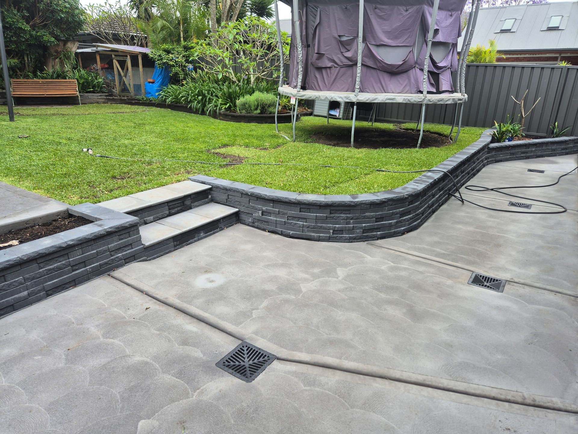 Gravel driveway bordered by stone steps and a small patch of green grass next to the road on a sunny day.