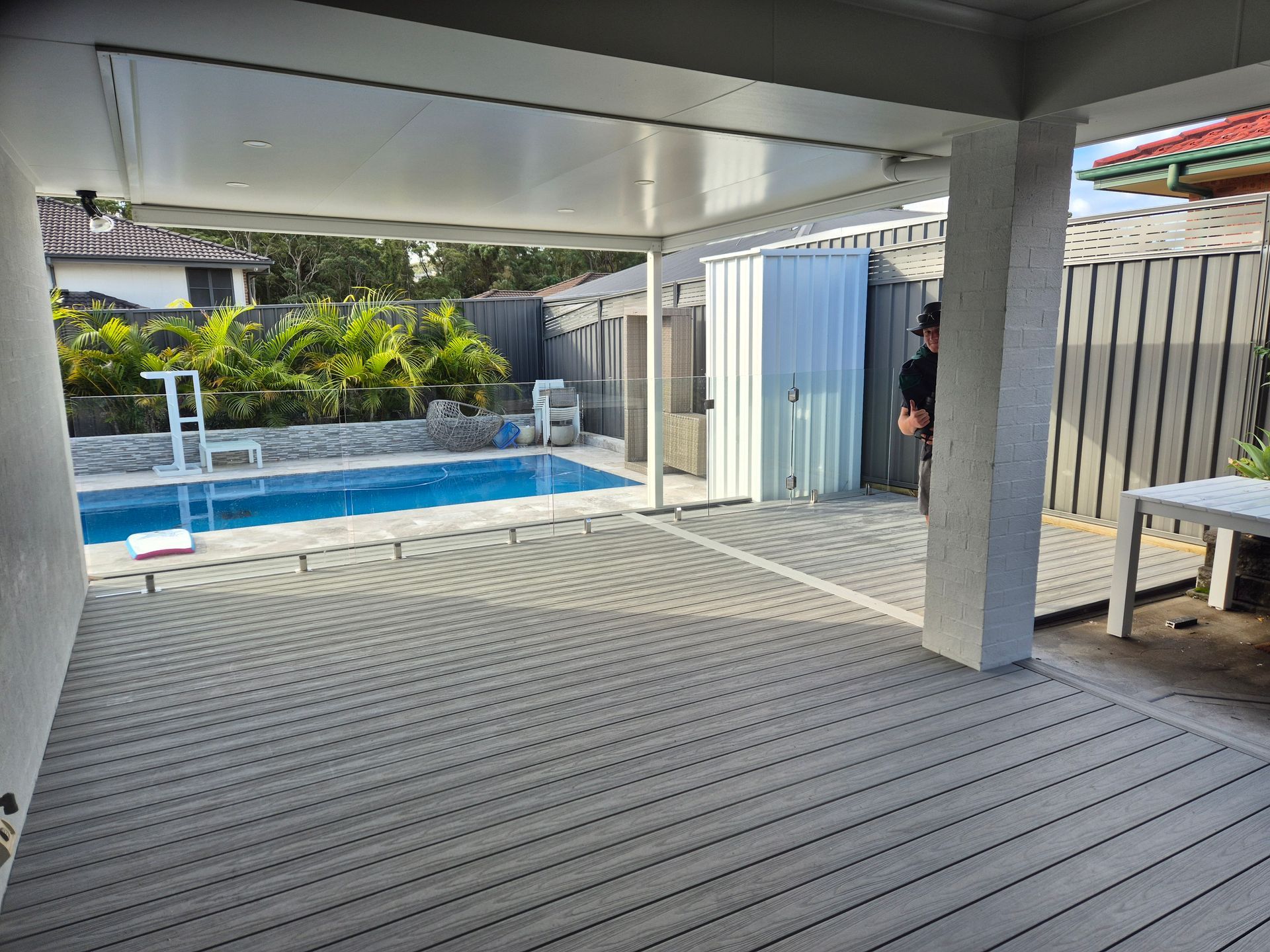 Covered patio with gray decking, pool in the background, and a storage shed.
