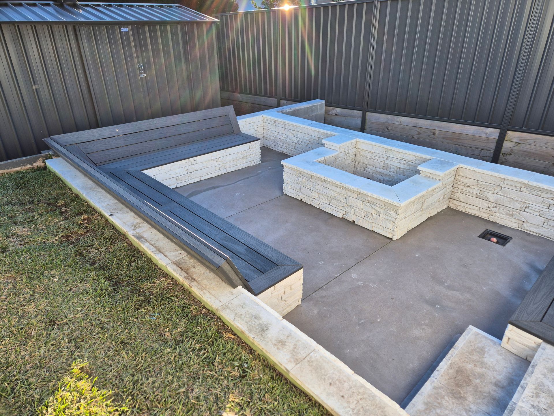 Outdoor patio with built-in seating and fire pit; concrete and stone construction, gray and white colors.