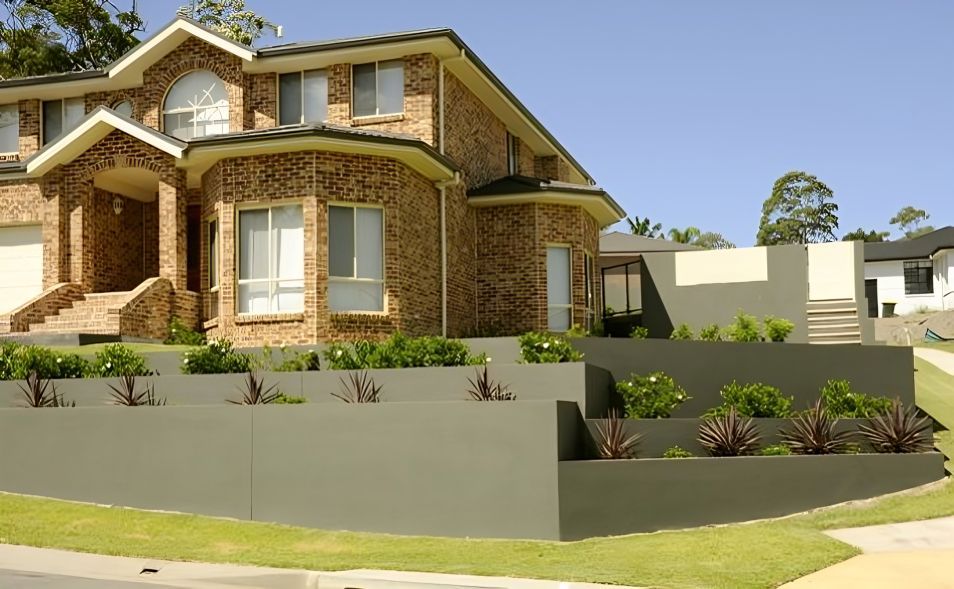 A Large Brick House Sits on A Lush Green Hillside — Creating Eden Landscaping In Boolaroo, NSW