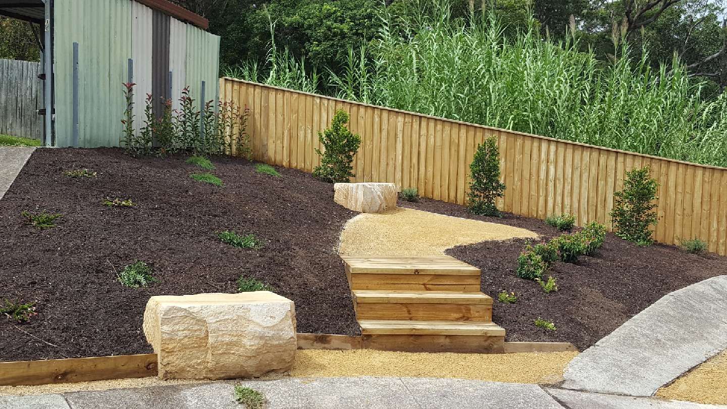 Stone steps and path ascend a landscaped hillside with a wooden fence and mulch.