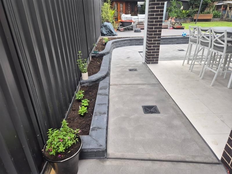 A retaining wall of gray stone borders a lawn; a sidewalk and street are in view.