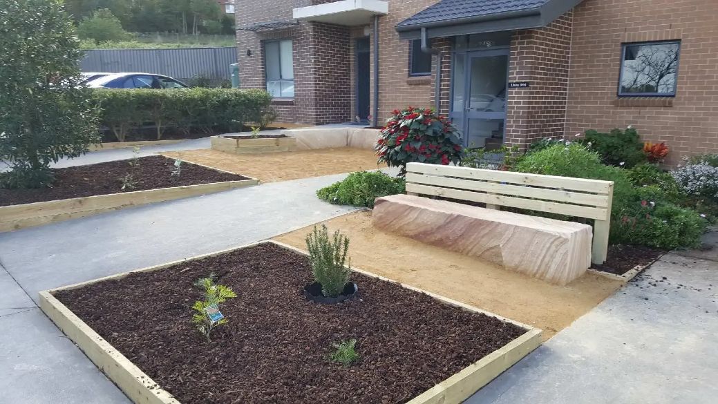 There Is a Bench in The Middle of A Garden in Front of A Brick Building — Creating Eden Landscaping In Teralba, NSW