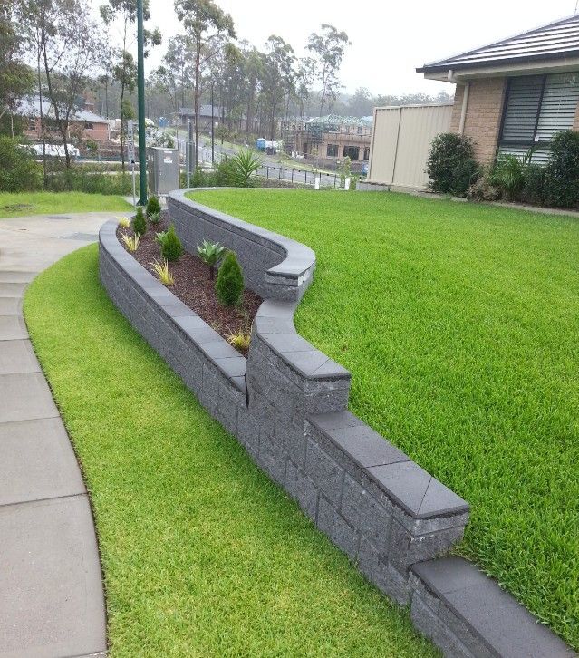 A Gray Stone Retaining Wall With Plants Divides a Green Lawn — Creating Eden Landscaping In Speers Point, NSW