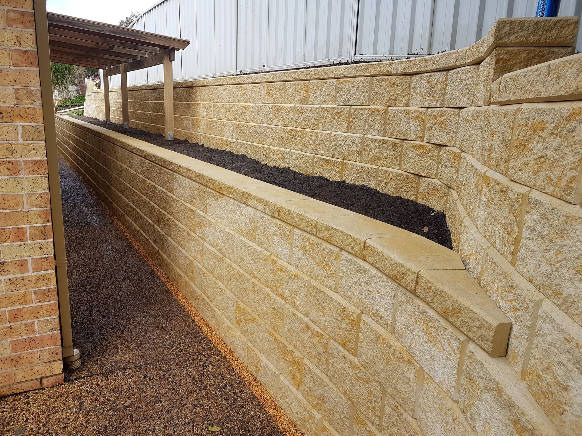 A backyard with a retaining wall, steps, and a green artificial lawn, enclosed by a white fence.