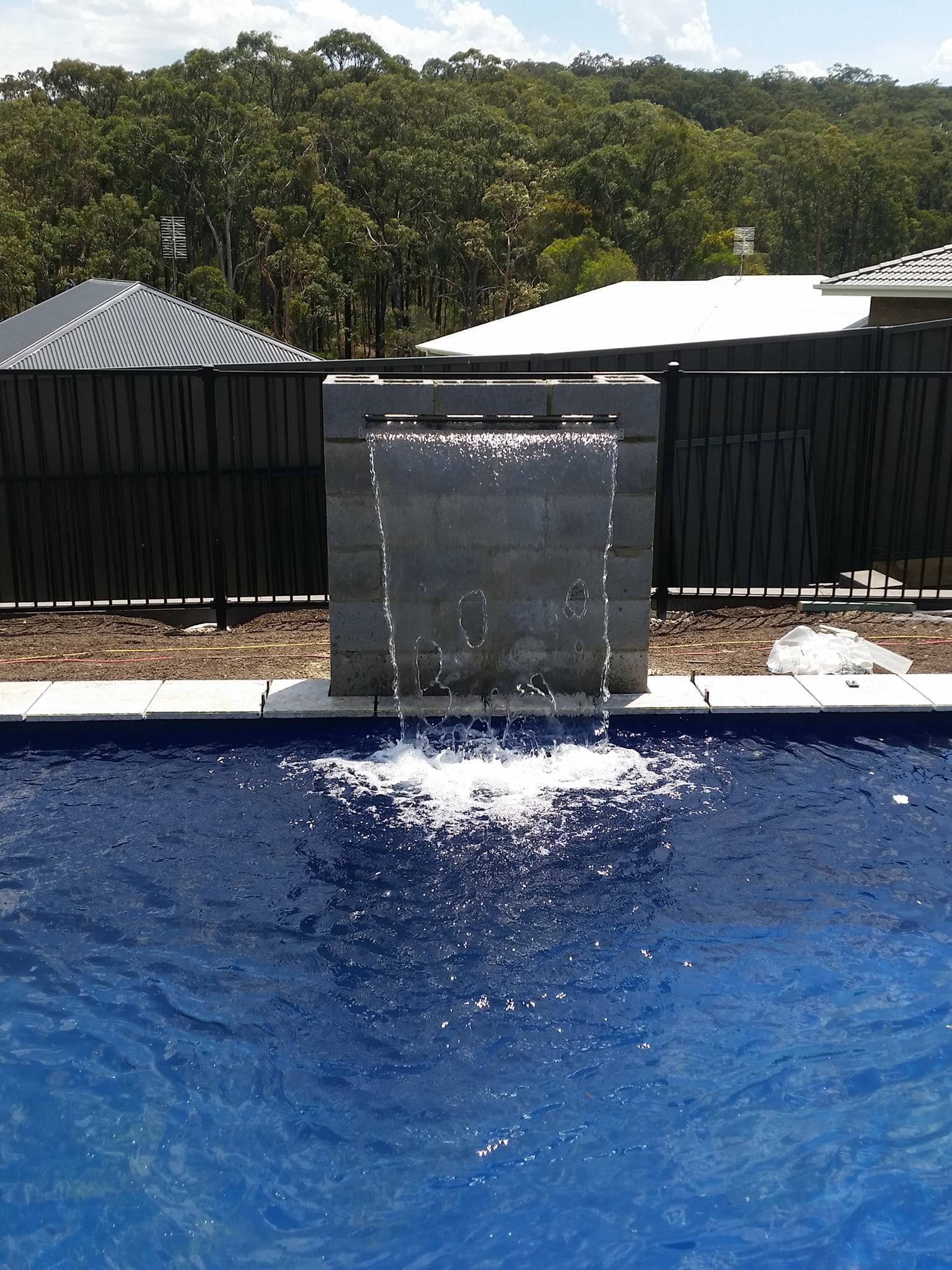 A water feature with a waterfall into a blue swimming pool.