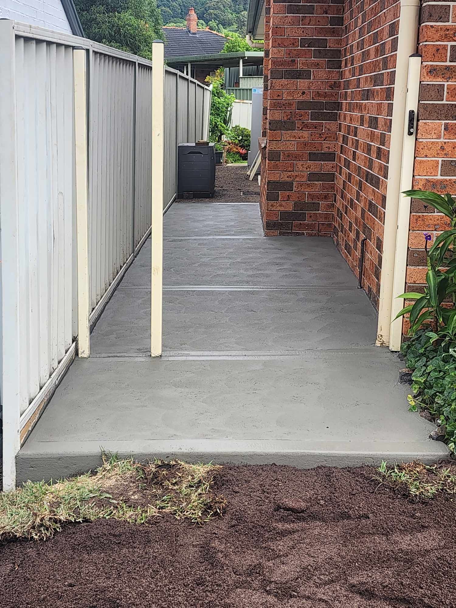 Concrete path between a brick wall and fence, with a trash can at the end — Creating Eden Landscaping In Edgeworth, NSW