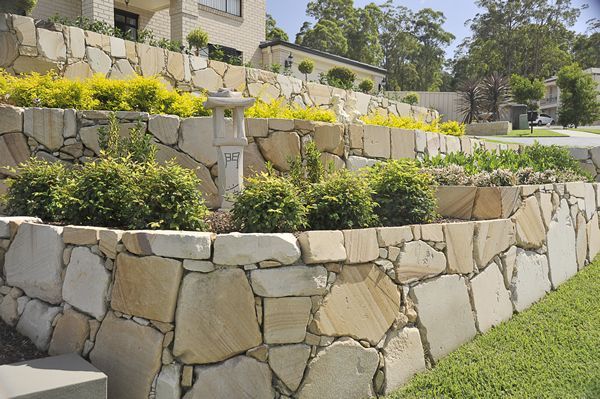 A Stone Wall with Plants Growing on It in Front of A House — Creating Eden Landscaping In Lake Macquarie, NSW