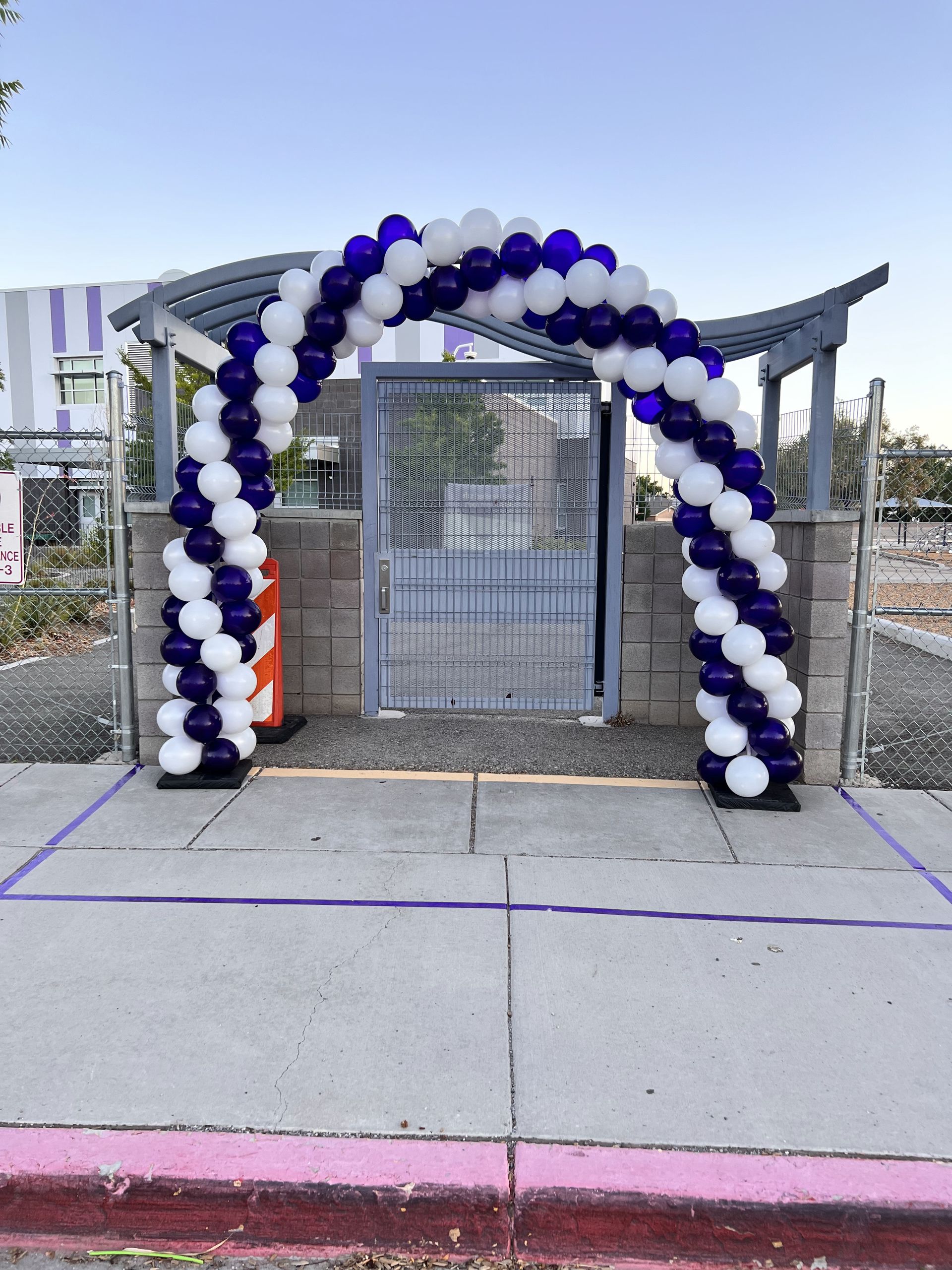 A purple and white balloon arch in front of a gate