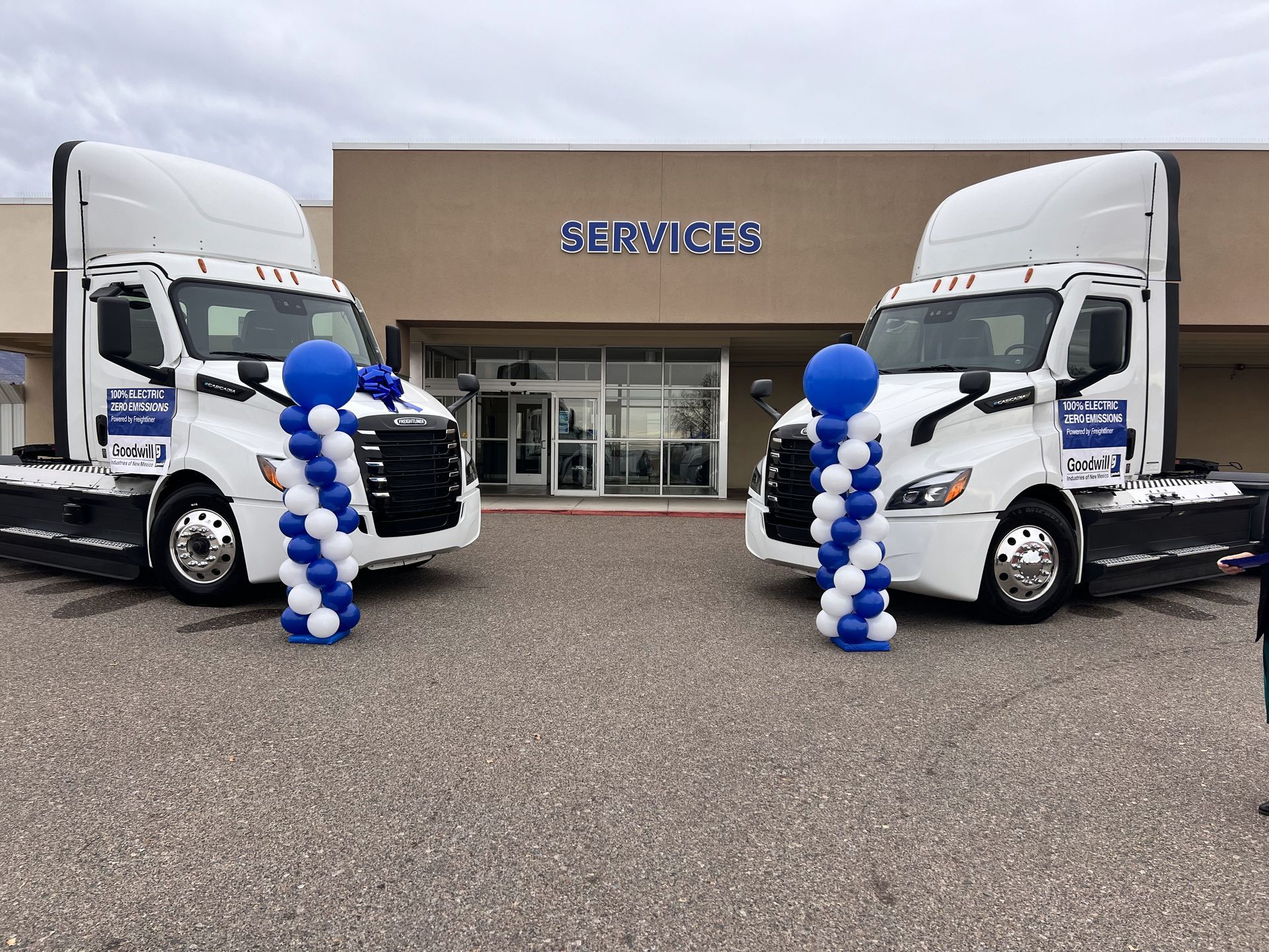 Two semi trucks are parked in front of a building with balloons on them.