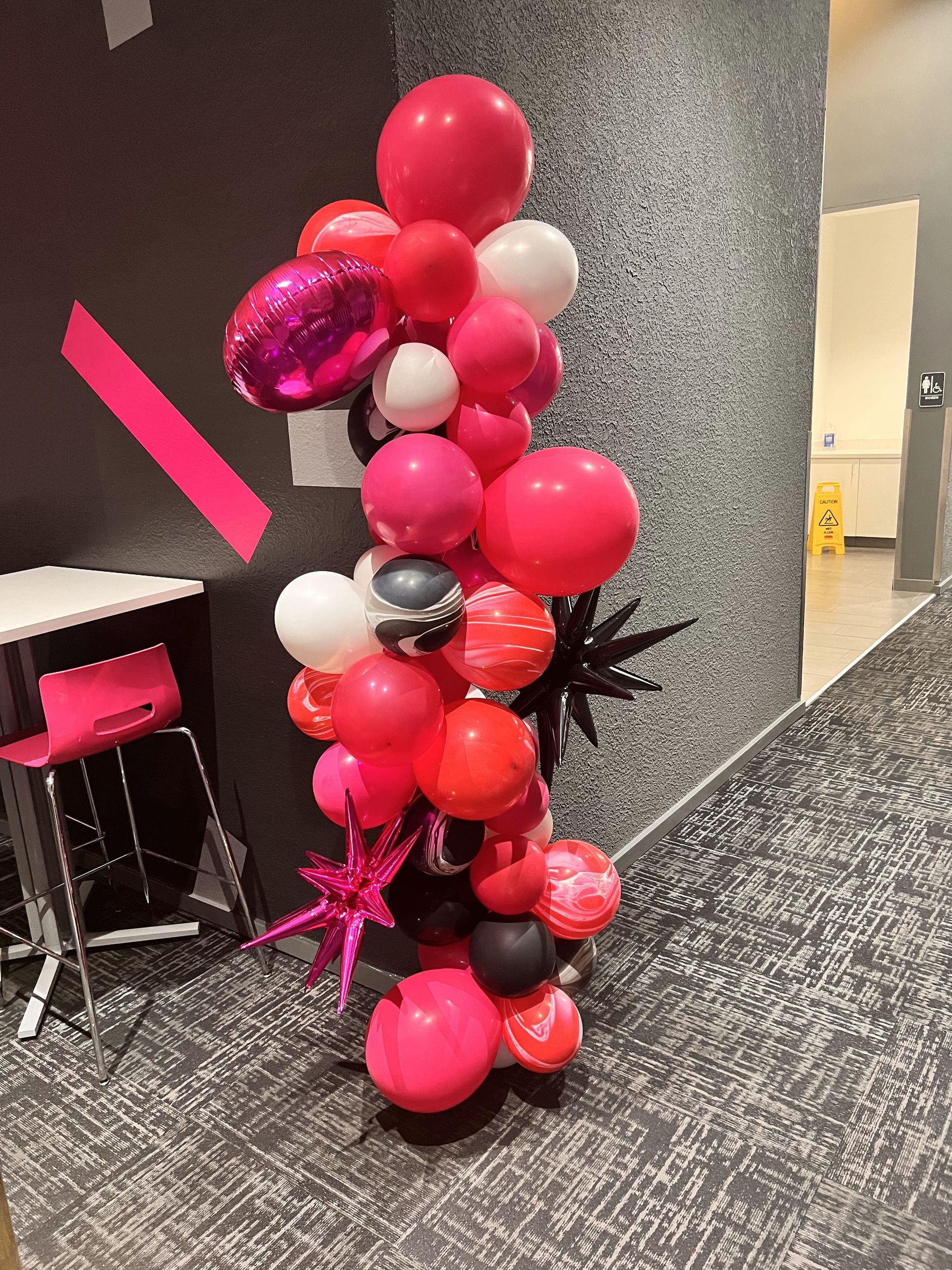 A bunch of balloons are sitting on the floor in a hallway.