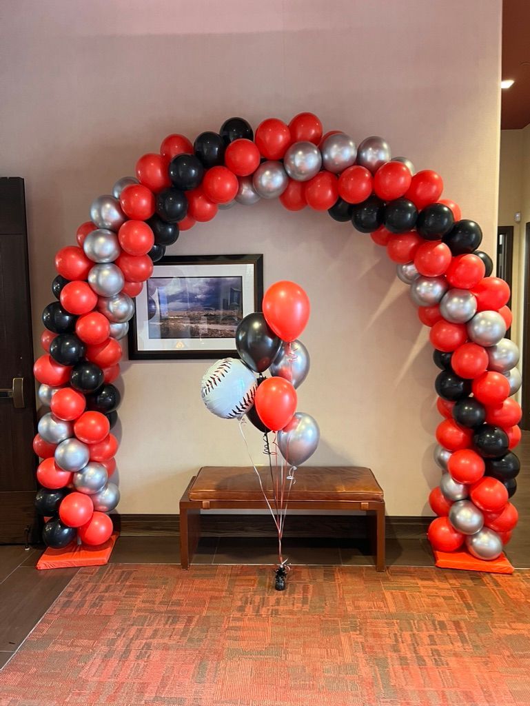 A red , black and silver balloon arch in a hallway.