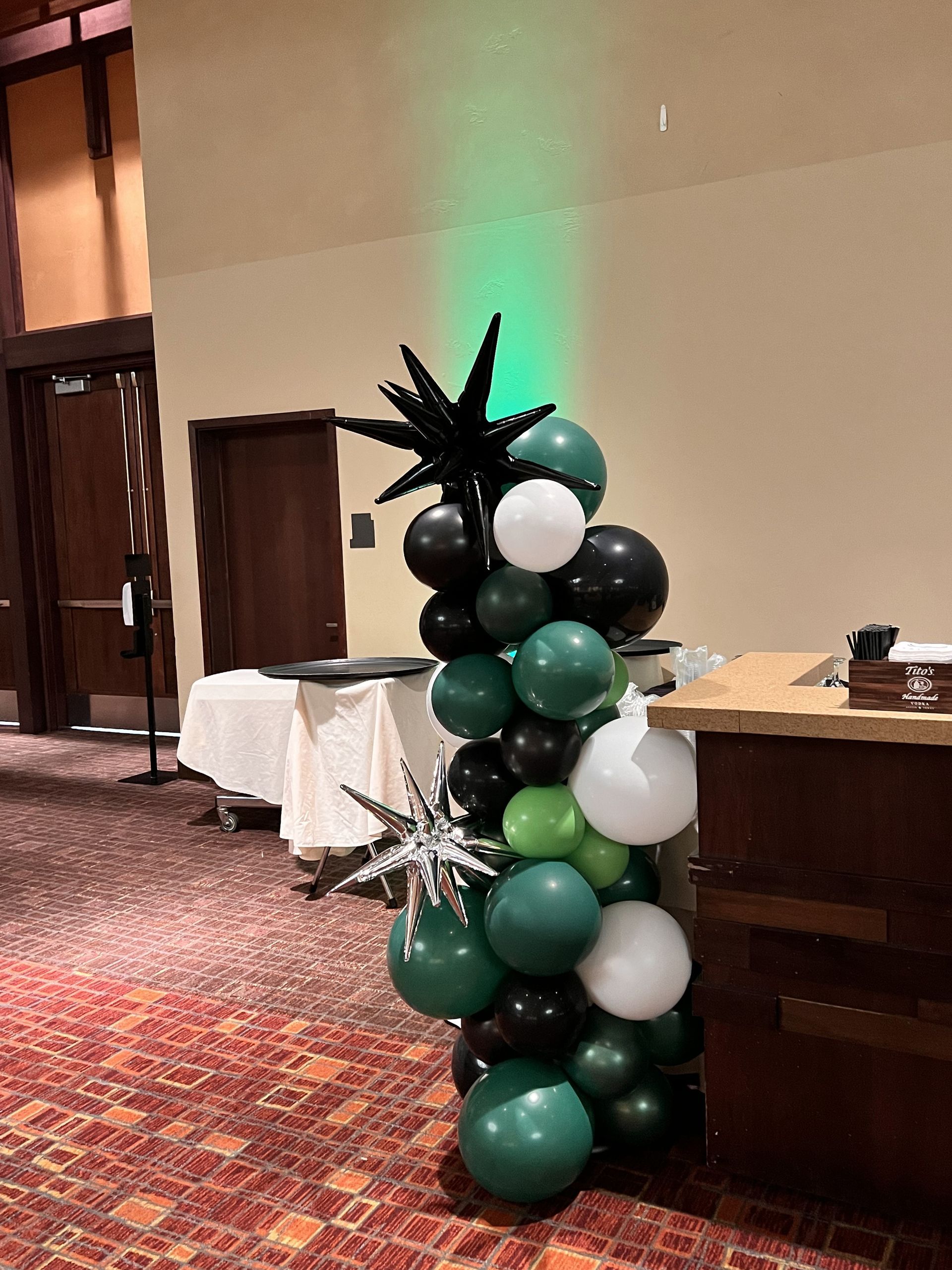 A tower of green , black and white balloons in a room.