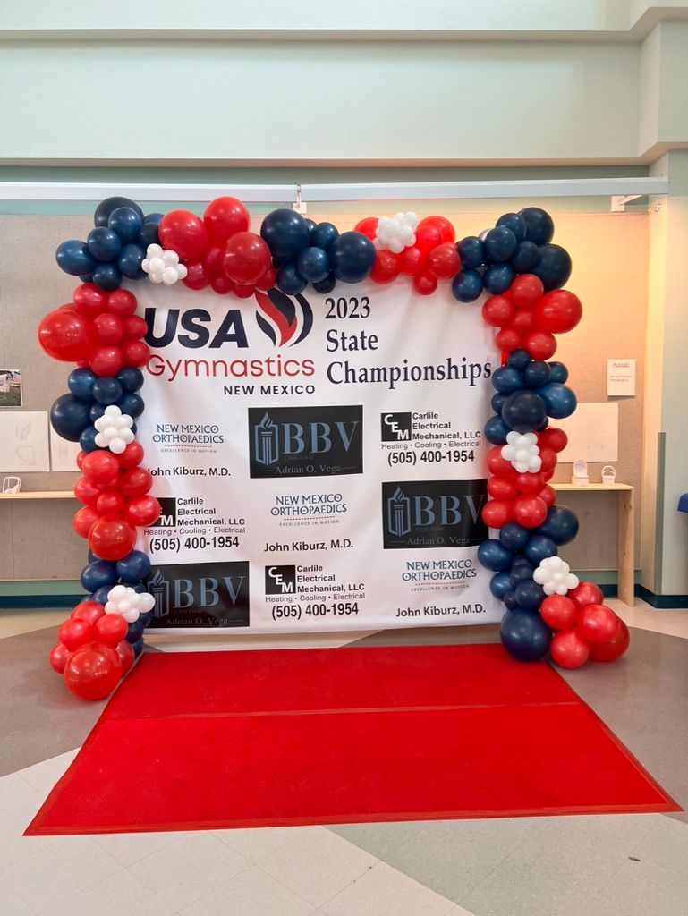 A red , white and blue balloon arch with a red carpet in front of it.