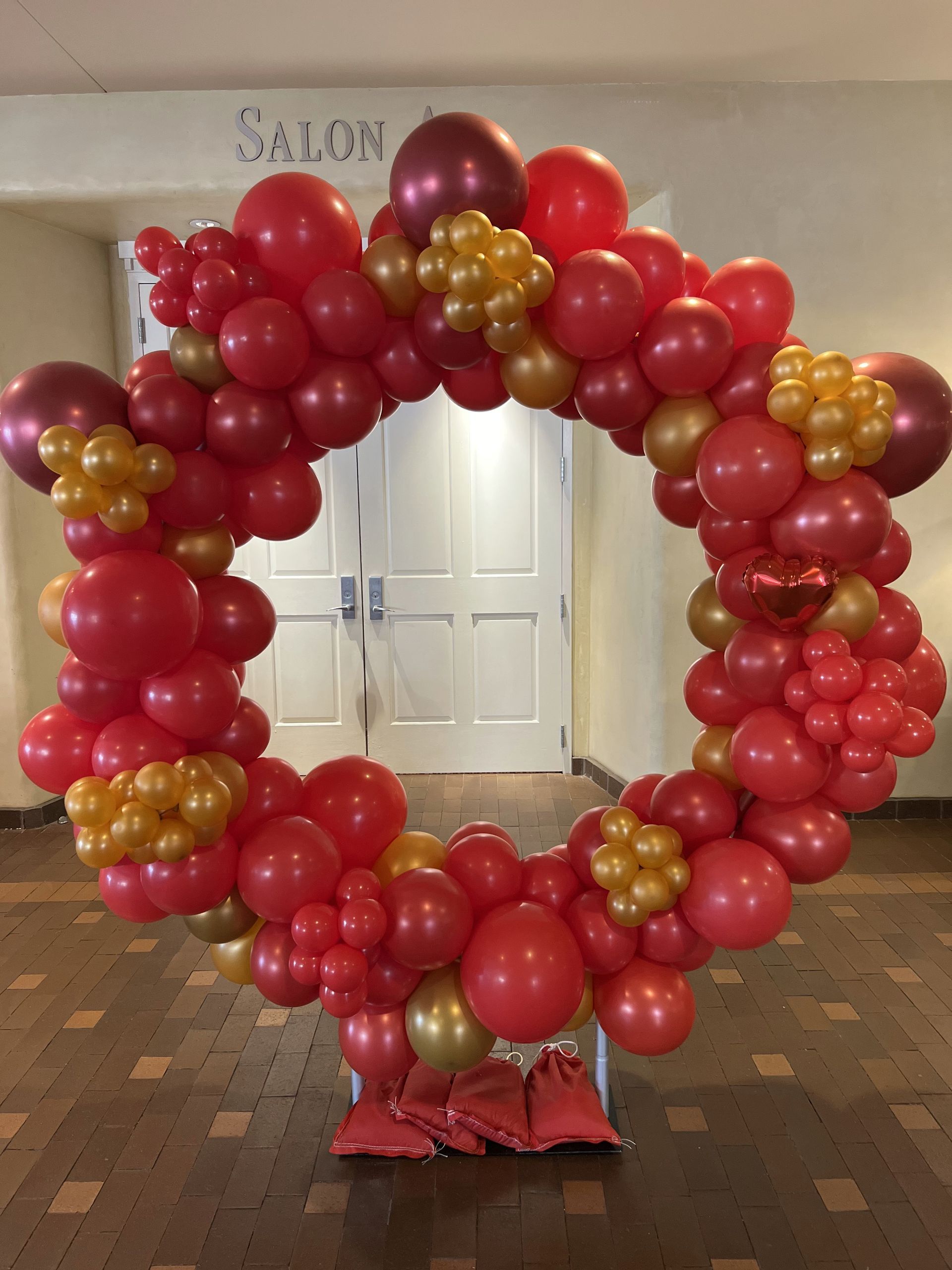 A circle of red and gold balloons in front of a door that says salon
