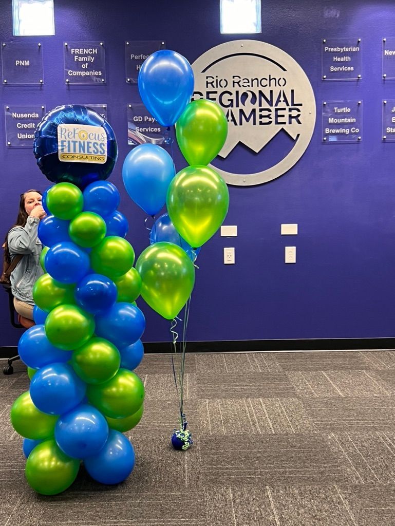A bunch of blue and green balloons on a pole in front of a purple wall.