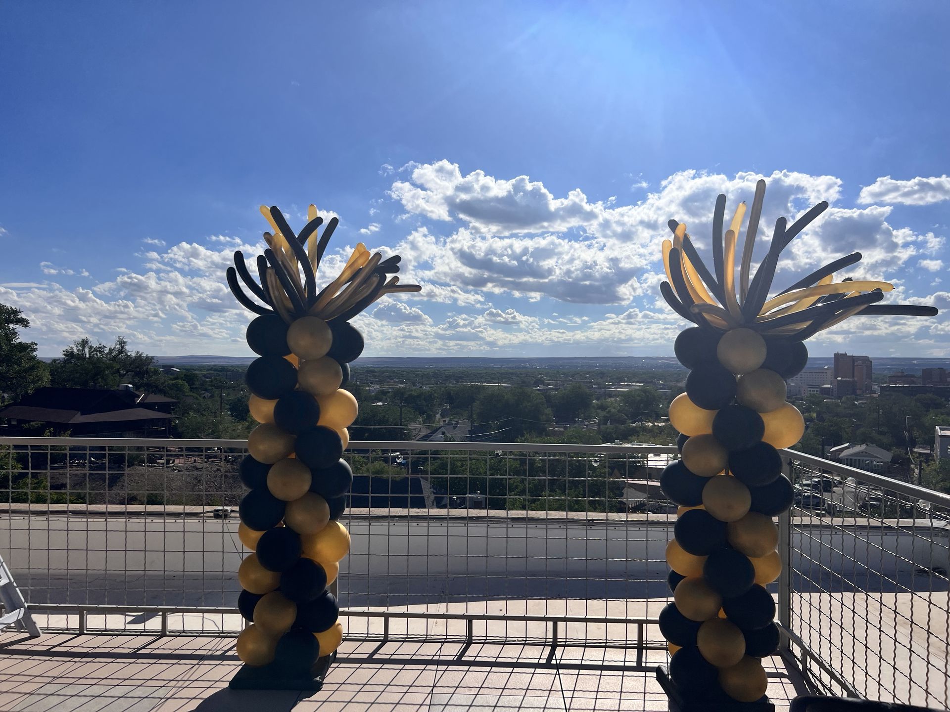Two black and gold balloon columns are sitting on a balcony overlooking a city.