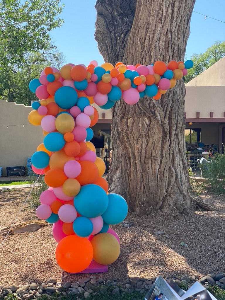 A bunch of colorful balloons are sitting next to a tree.