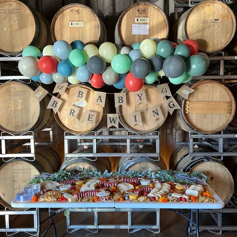 A table with food and balloons in front of a wall of wooden barrels.