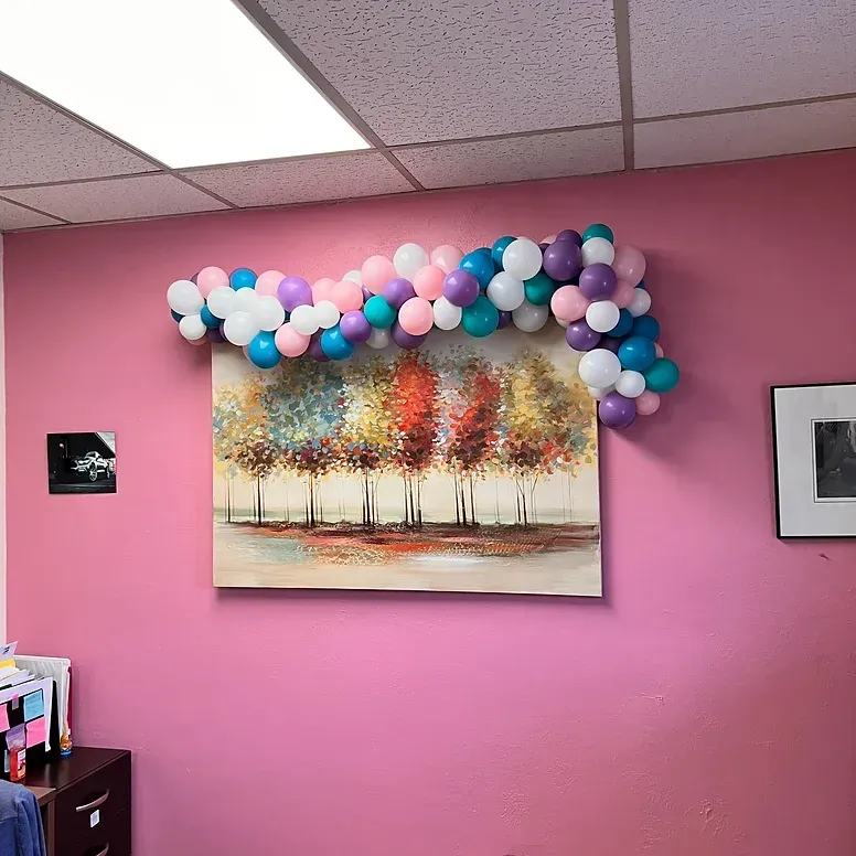 A pink wall with a painting and balloons on it