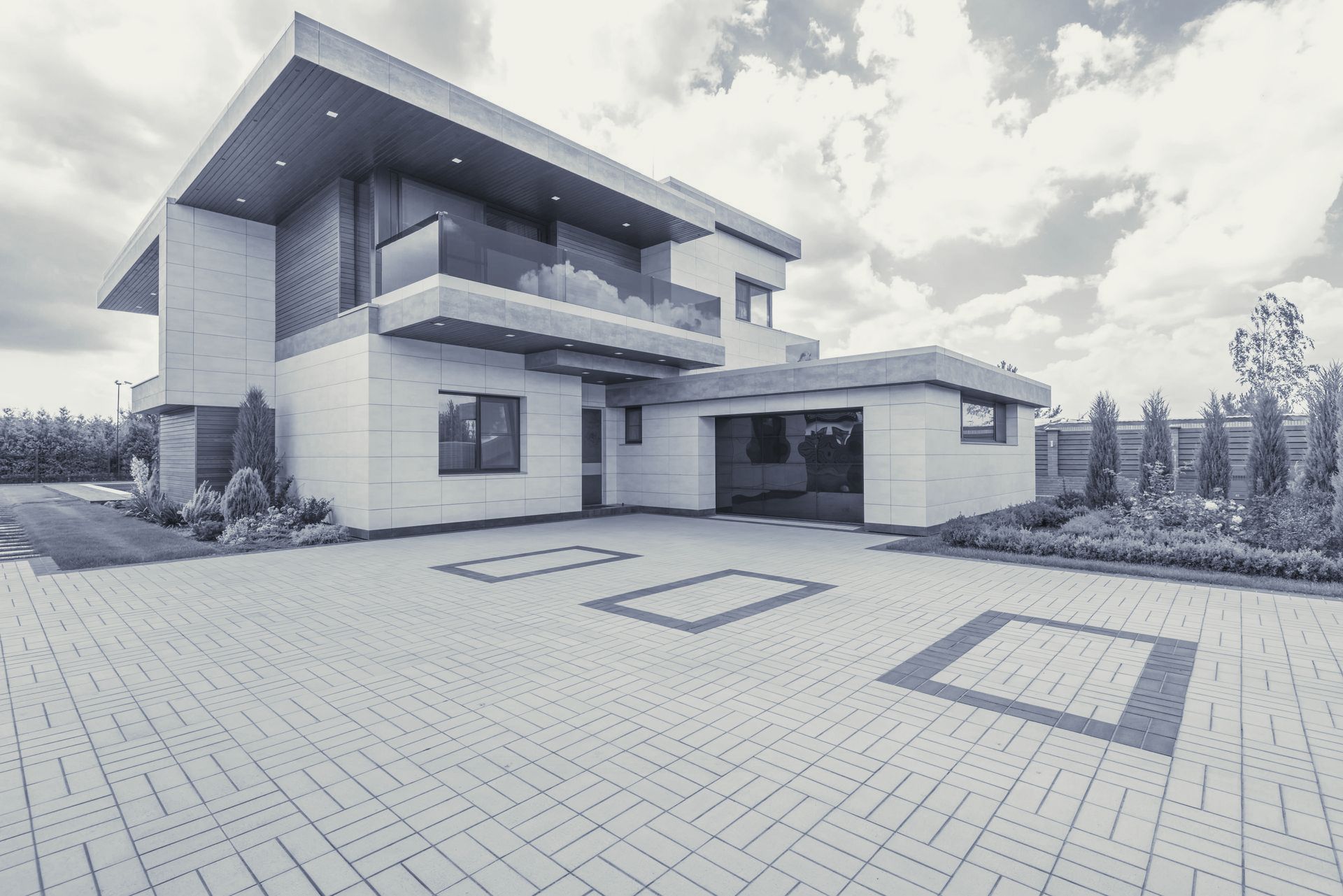 A large modern house with a brick driveway in front of it.