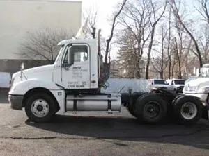 White semi-truck parked outdoors, side view. Cab with fuel tank and rear wheels visible.