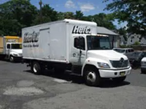 White Hertz box truck parked on a street in front of buildings.