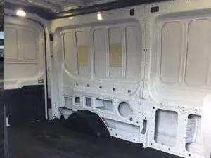 Interior of a white van with bare walls and floor, showcasing structural features and a dark floor covering.