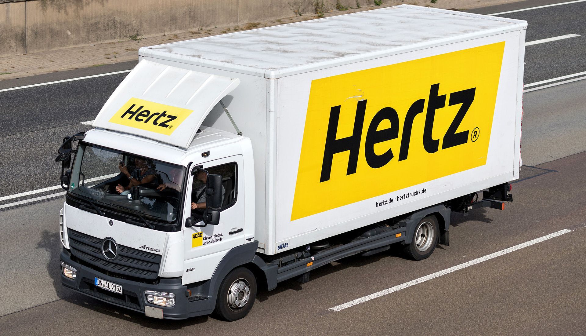 White Hertz truck driving on a highway, with large yellow 