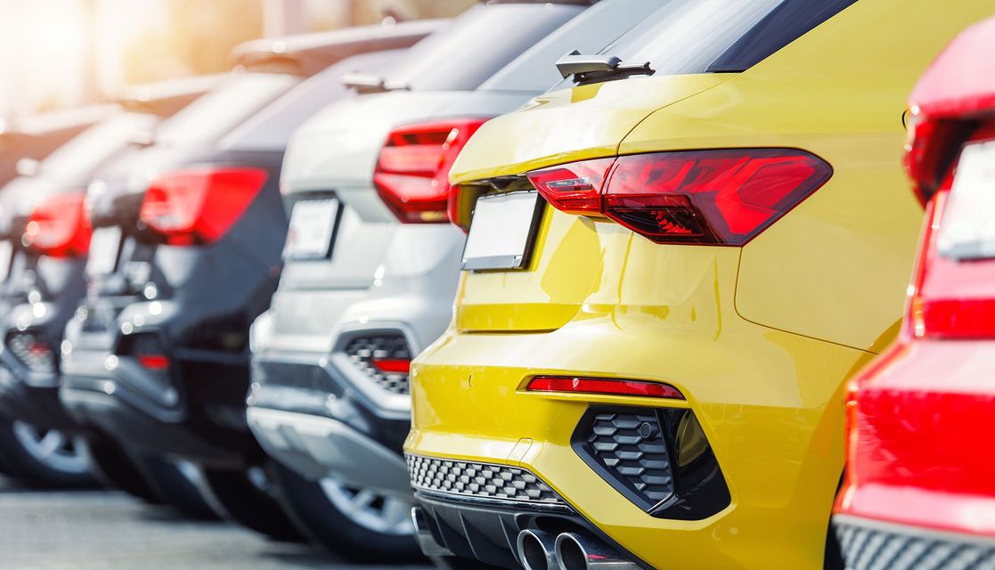 Row of cars, varying colors (yellow, black, silver, red), parked in a line, rear view.