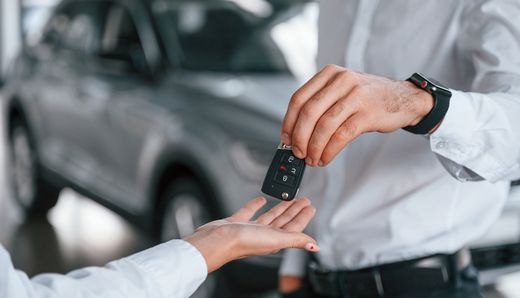 Person handing car keys to another person near a gray car.
