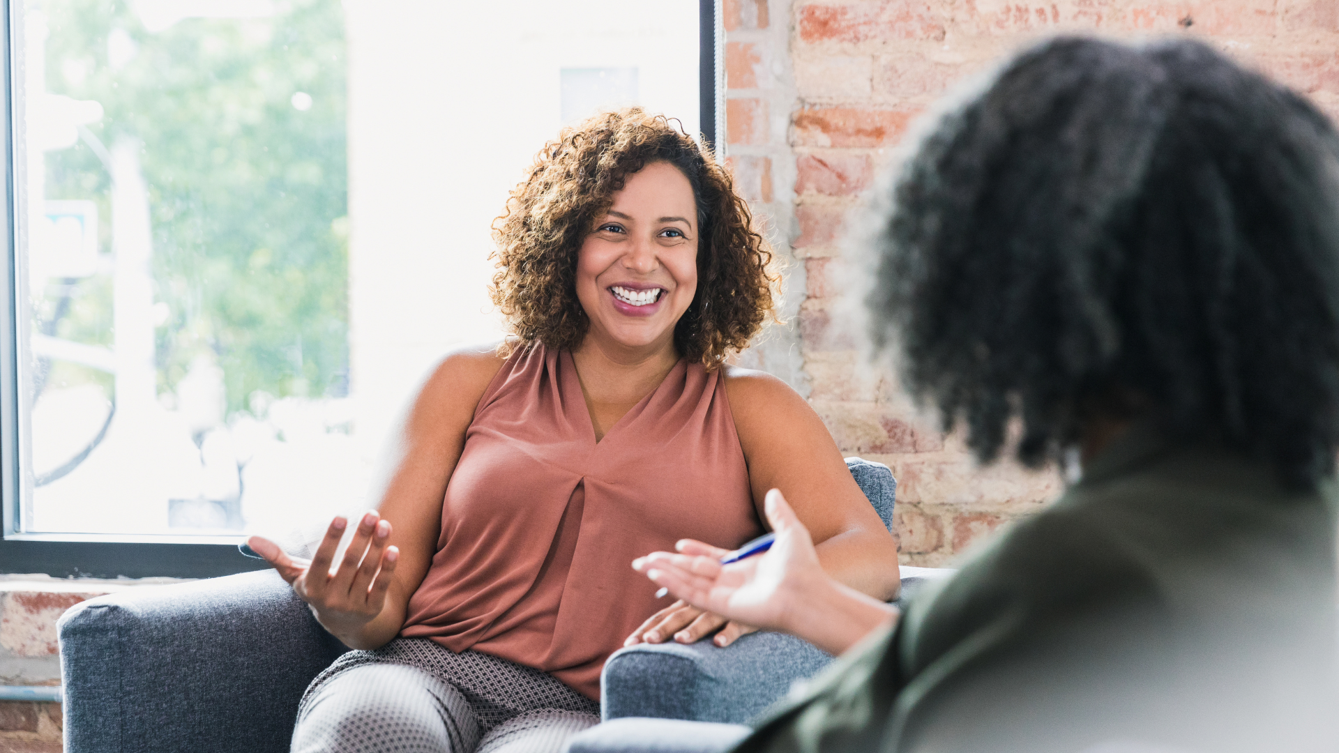 A man is sitting on a couch talking to a woman who is holding a clipboard.