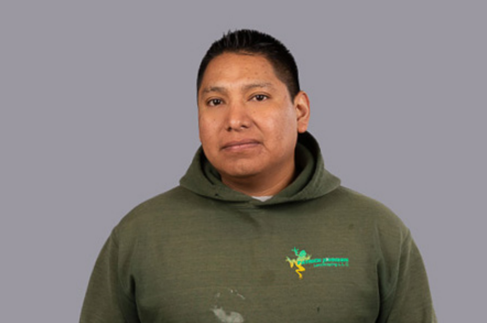 A man in a green hoodie is standing in front of a gray background.