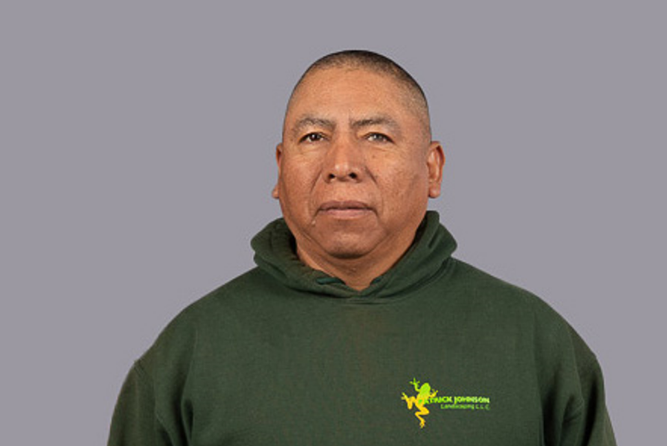 A man in a green hoodie is standing in front of a gray background.