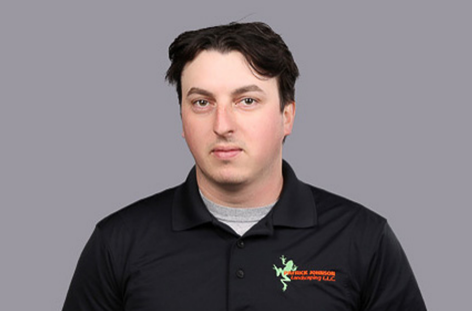 A man in a black shirt is standing in front of a gray background.
